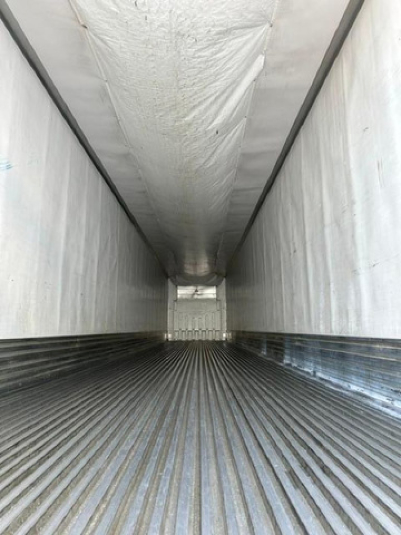 Inside a refrigerated trailer cargo area showing ribbed metal floor and white walls with ceiling insulation visible.