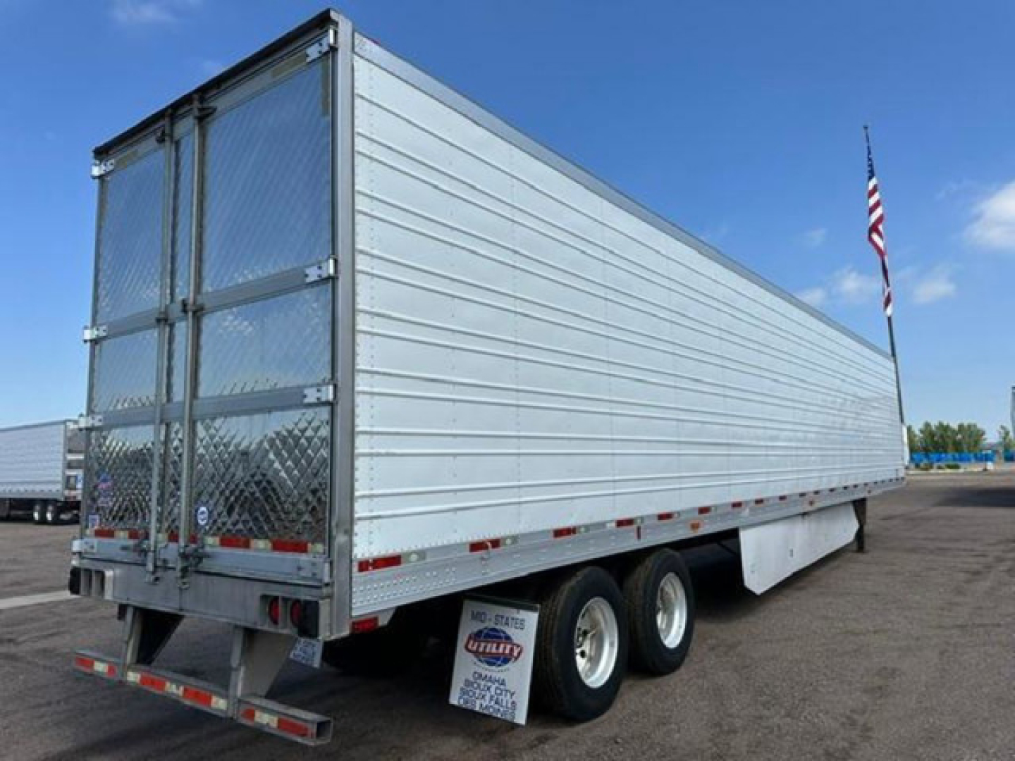 Rear and side view of a 2016 utility refrigerated trailer (reefer) with metal ribbed panels, dual rear doors, diamond plate gate, and spare tire undercarriage. Visible text on a small plate near the back shows stock number and dealer markin