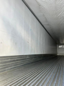 Trailer interior showing corrugated metal floor and side walls of a refrigerated trailer.