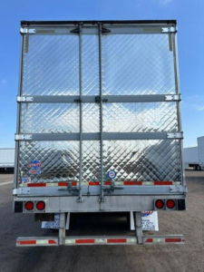 Refrigerated trailer rear showing diamond plate aluminum doors and rear bumper with red/white reflective tape.