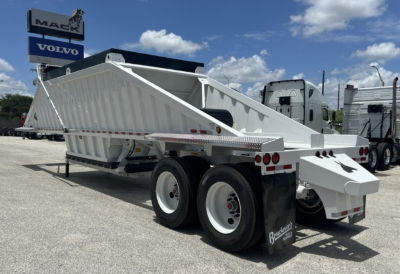 Dump trailer in a yard showing a white BDT-40 style end dump with dual rear axles and plywood bed sides, brand decals, and a Maek/ Volvo dealership sign in background.