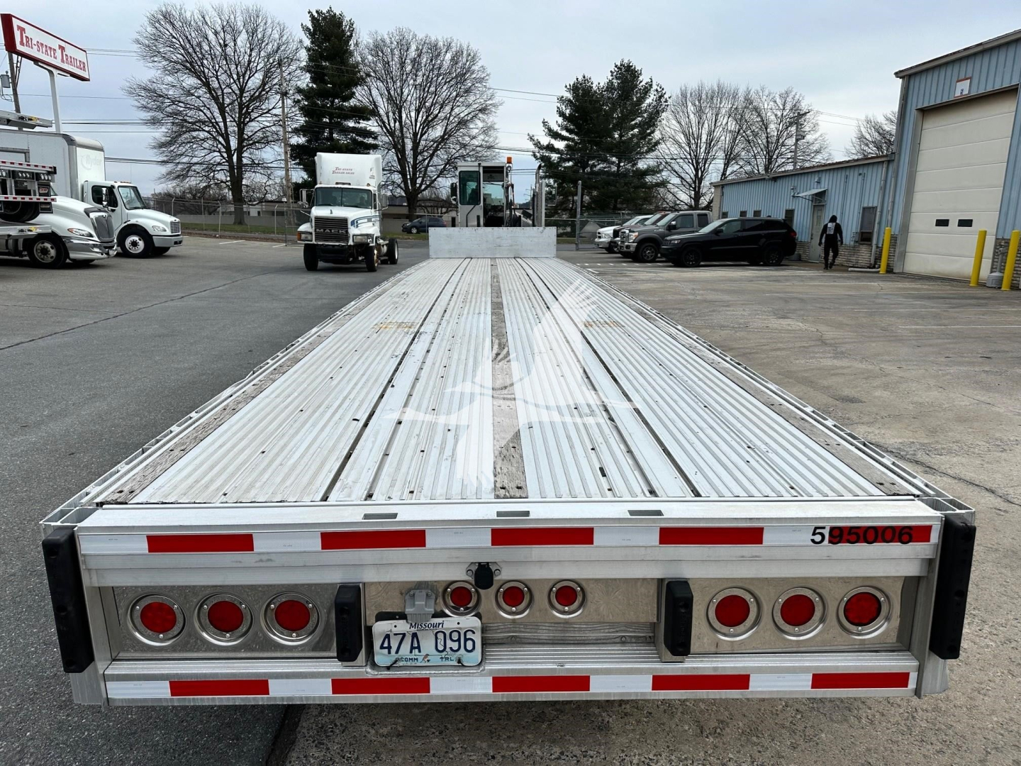 Trailer bed of a used 2019 Reitnouer drop-deck trailer showing rear end with taillights, license plate 47A 096, and stock number 595006.