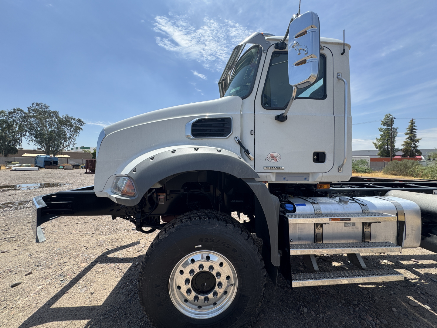 Truck cab and chassis section of a 2027 Mack GR44B showing front wheel, chrome fuel tanks, and side mirror.