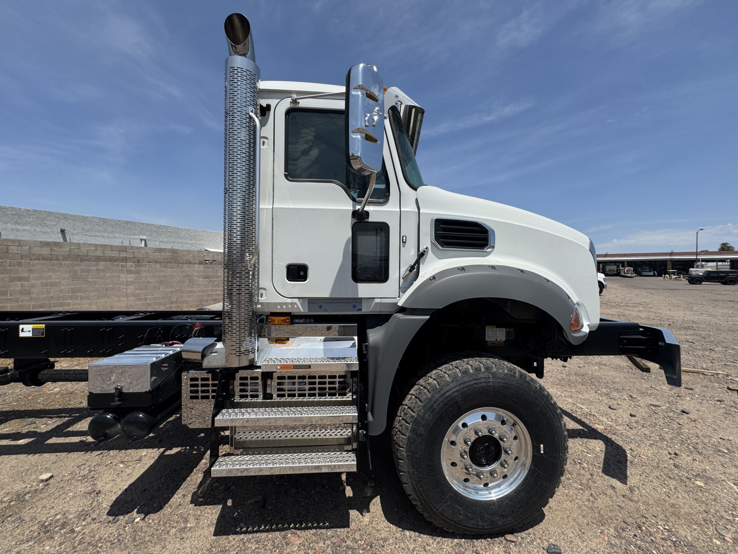 Truck cab and chassis side view showing metallic steps, vertical exhaust stack, and front wheel. Visible text on components not legible.