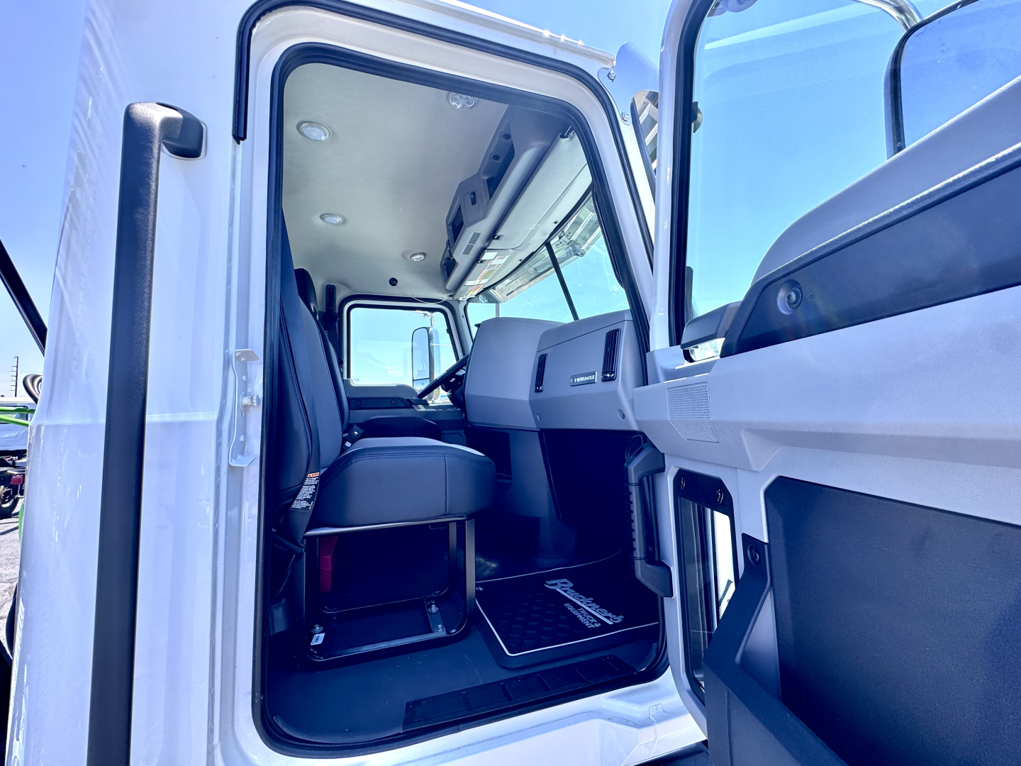 Cab interior of a 2027 Mack PI64T truck showing seating area and dashboard from open door