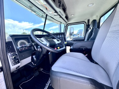 Truck cabin interior of a 2027 Mack PI64T showing steering wheel, dashboard with gauges, driver seat, and passenger seat.