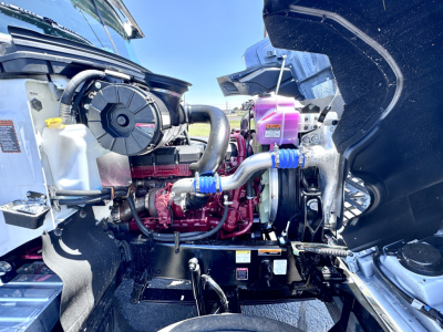 Engine bay of a new 2027 Mack PI64T truck showing coolant reservoir, pink coolant, hoses, and turbo/intercooler components.