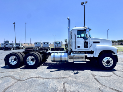 Truck side view showing 2027 Mack PI64T conventional daycab with three rear axles and fuel tanks, chrome steps, and white cab.