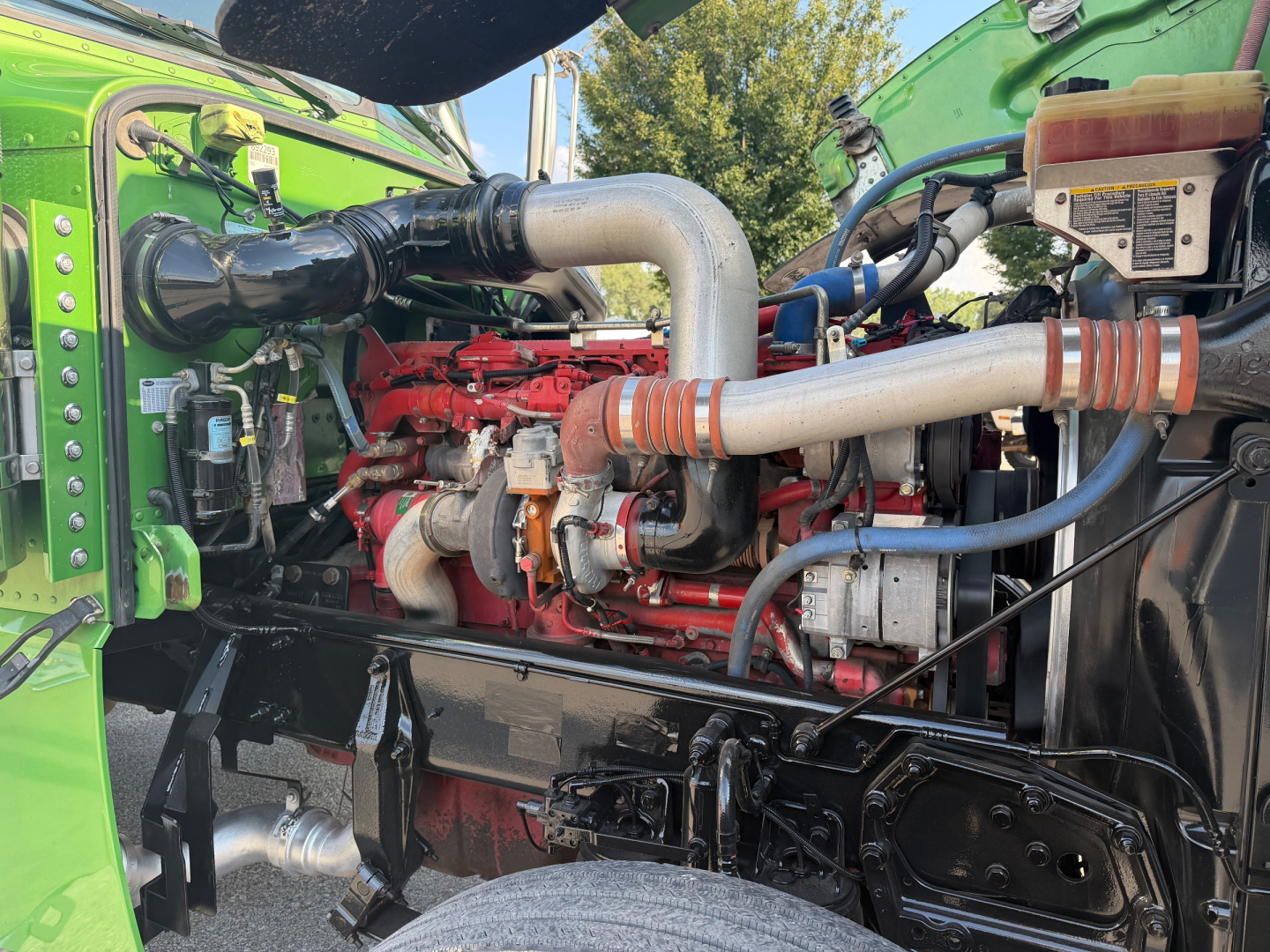 Peterbilt 389 engine bay showing large intake pipe, red engine block, and various hoses and reservoirs.