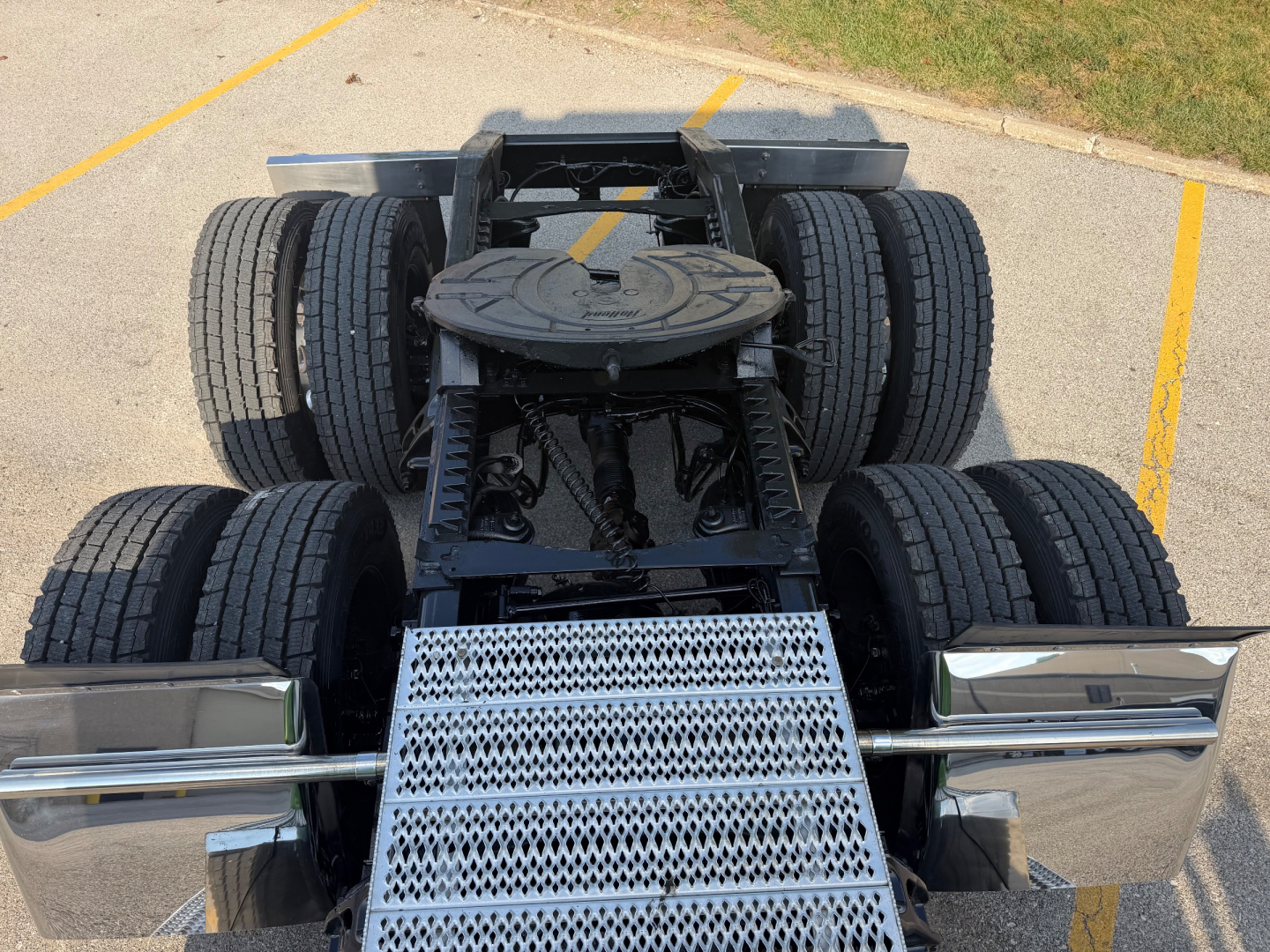 Truck chassis rear view showing fifth wheel, dual rear axle with four tires, metal fuel tank step, and chrome bumper; Peterbilt 389 cab not visible.