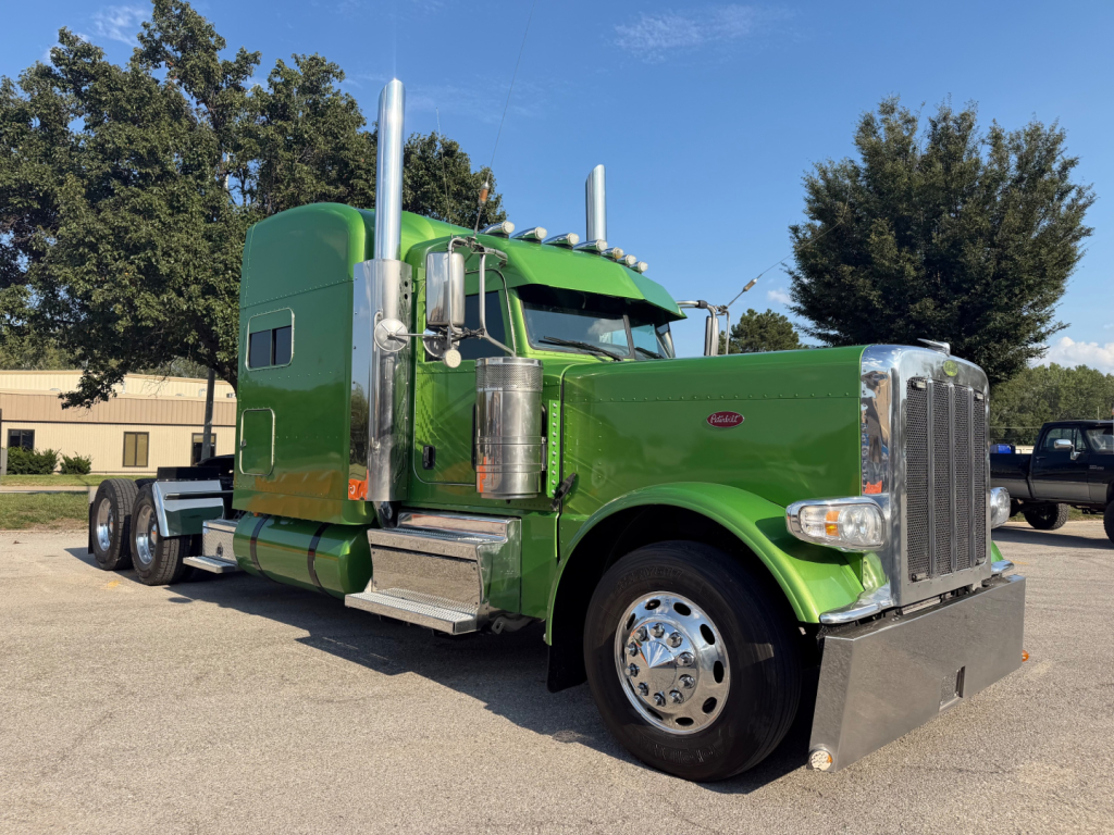 Peterbilt 389 conventional sleeper truck in green, front-right view showing chrome grille, large air intakes, dual exhaust stacks, and aluminum steps.