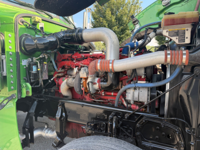 Peterbilt 389 engine bay showing large intake pipe, red engine block, and various hoses and reservoirs.