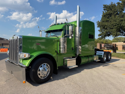 Peterbilt 389 sleeper cab truck in green, front-left view showing chrome exhaust stacks and grille.