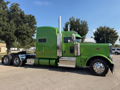 Green Peterbilt 389 truck tractor side view showing sleeper cab, chrome exhaust stacks, dual rear axles, and polished wheels.