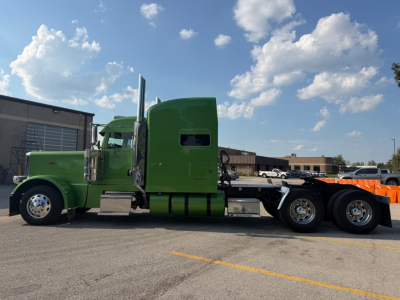 Peterbilt 389 truck in green cab with sleeper and dual rear axles viewed from side.