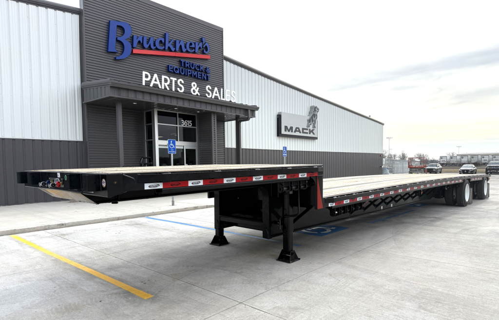 Flatbed trailer showing a 48' spread drop deck with black-painted deck and support stands in a dealership lot.