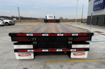 Trailer rear view of a 2027 Dura Haul drop deck 48' spread trailer showing red/white reflective tape, taillights, mud flaps with Dura-Haul logo, and a dealership building in the background.