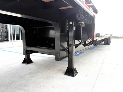 Drop deck trailer landing gear and underside view showing black steel framework and support legs with feet on concrete.
