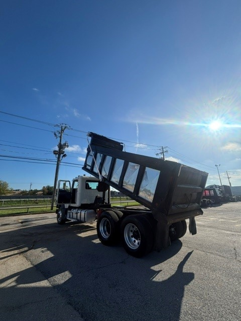 Dump truck in service showing a Mack GRANITE dump bed raised for dumping with white cab and black dump body.