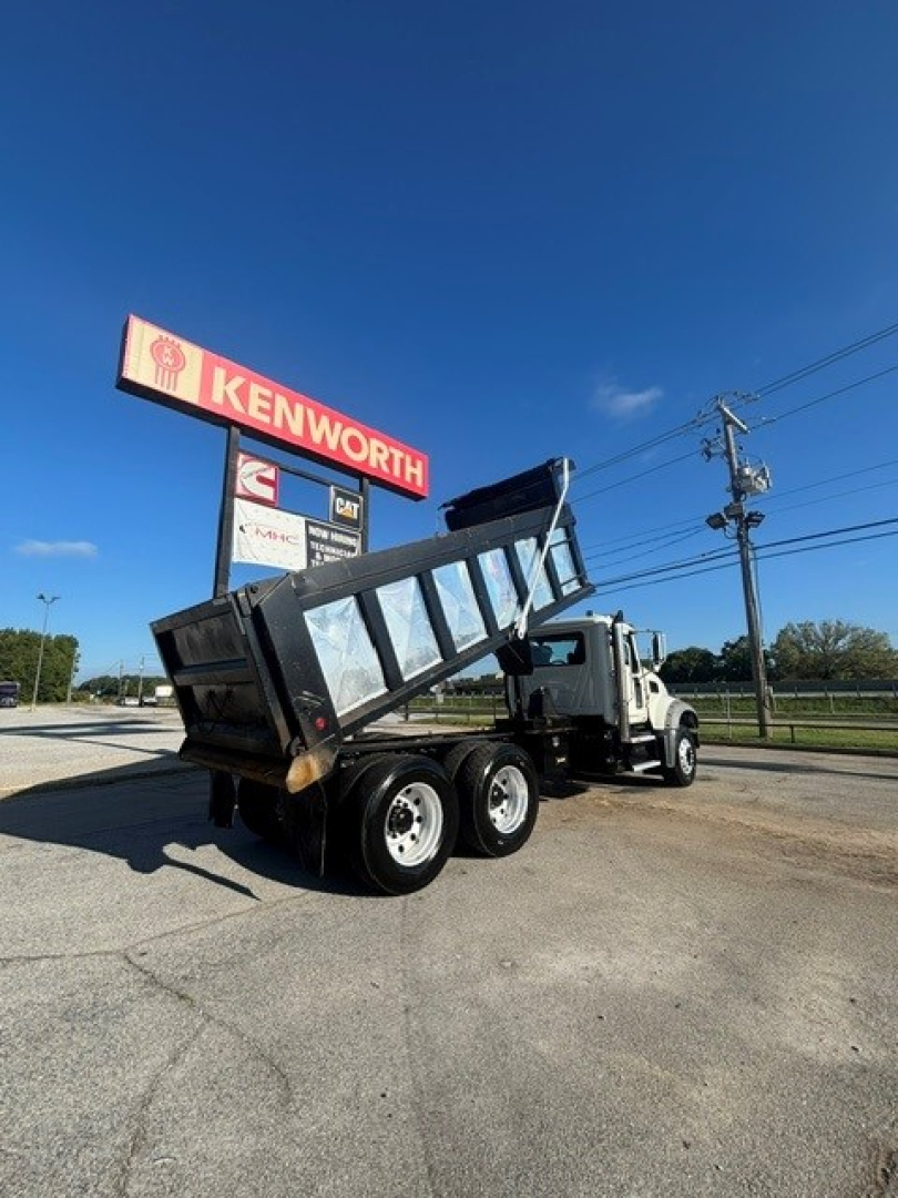Dump truck chassis with raised dump bed showing Mack Granite truck and Kenworth sign in background.