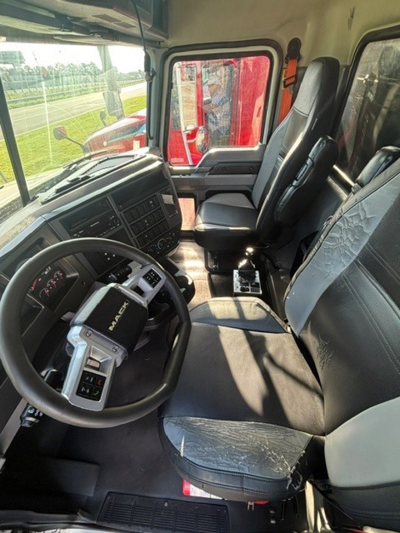 Interior of a Mack Granite truck cab showing steering wheel, dashboard, and seats. Visible controls on the center console and driver seat area; appears clean with fabric seats.