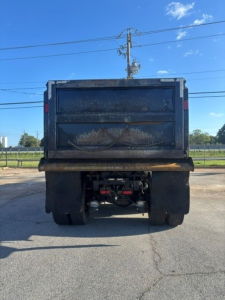 Dump truck rear showing cargo bed and dual rear wheels with hydraulic system under the bed.