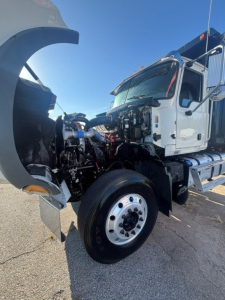 Front-left view of a 2022 Mack Granite dump truck with hood open, showing engine bay components, air intake, hoses, and front wheel.
