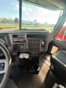 Truck cab dashboard interior showing steering wheel, center console, stacked gauges, HVAC controls, and cup holders.
