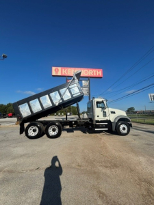 Dump truck in-service with dump bed raised, Mack Granite model. Visible text includes IK E NORTH sign in background and dump bed with metallic panels.