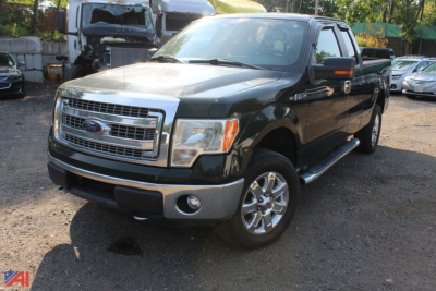 Ford F-150 pickup truck in a used lot, green body, chrome grille, four-door crew cab, running boards visible.