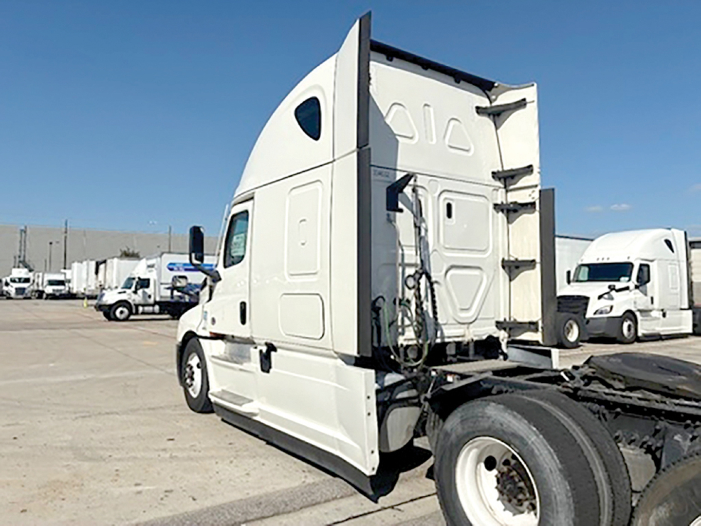 Truck cab side-view of a white Freightliner Cascadia126 sleeper tractor showing the back of the cab and rear wheel area.