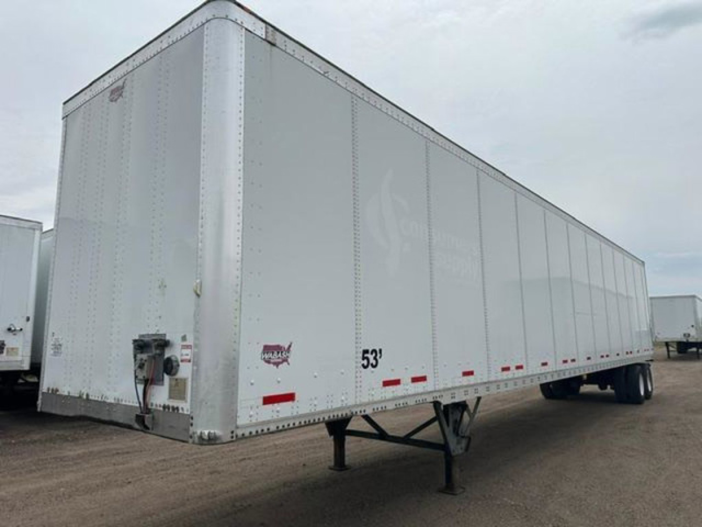 Trailer side view showing a 53' white aluminum van trailer with wheel drops and entry door, no visible branding.