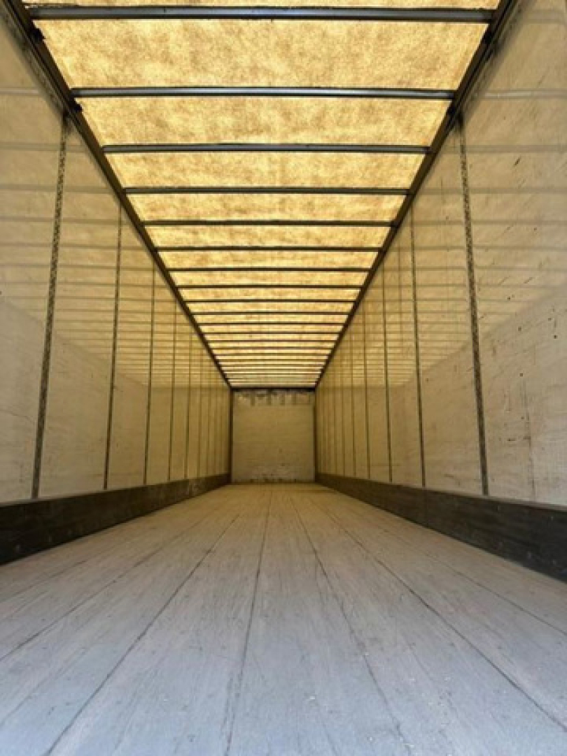 Van trailer interior cargo area with long rectangular ceiling lights, empty wooden floor, side walls, and rear door visible in distance.