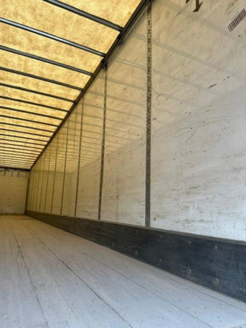 Trailer interior showing empty cargo area with vertical rails and side walls, no visible branding, long empty floor, light from translucent roof panels.