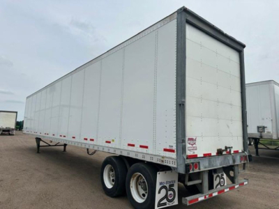 Trailer side view showing a white Wabash van trailer with rear rollers and dual rear axles.