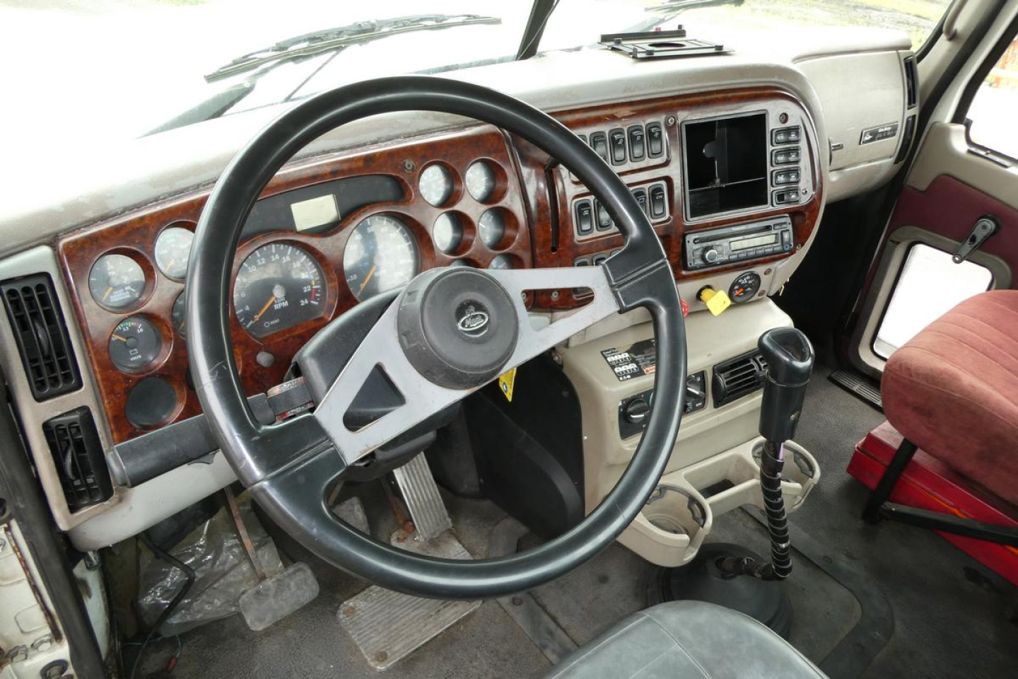 Dashboard area of a Mack CHN613 truck showing steering wheel, instrument cluster, wood grain dash, radio,Climate controls, and gear shifter.