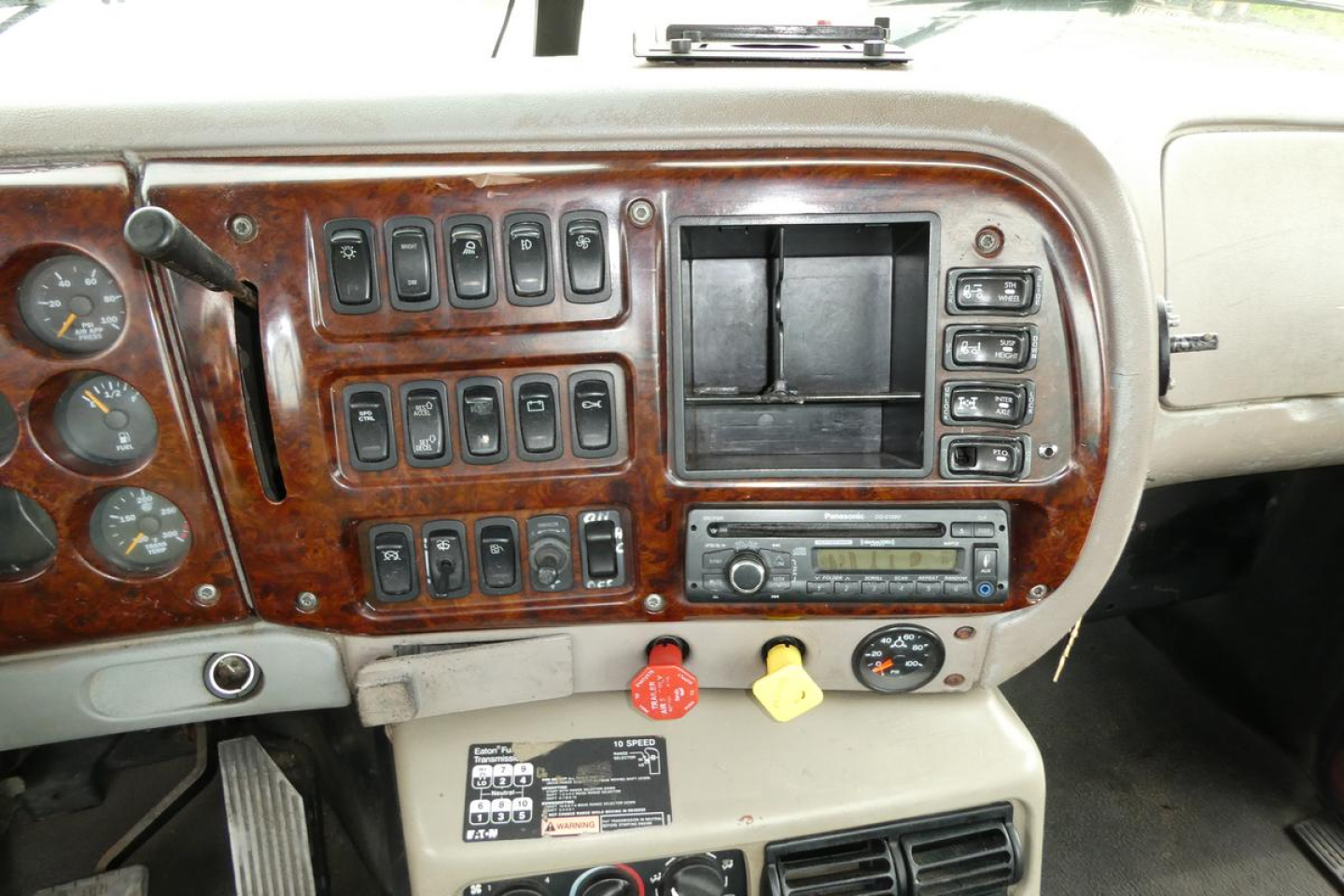 Mack CHN613 dashboard panel showing multiple switches, gauge cluster, center storage, and radio in a woodgrain trim truck cabin.