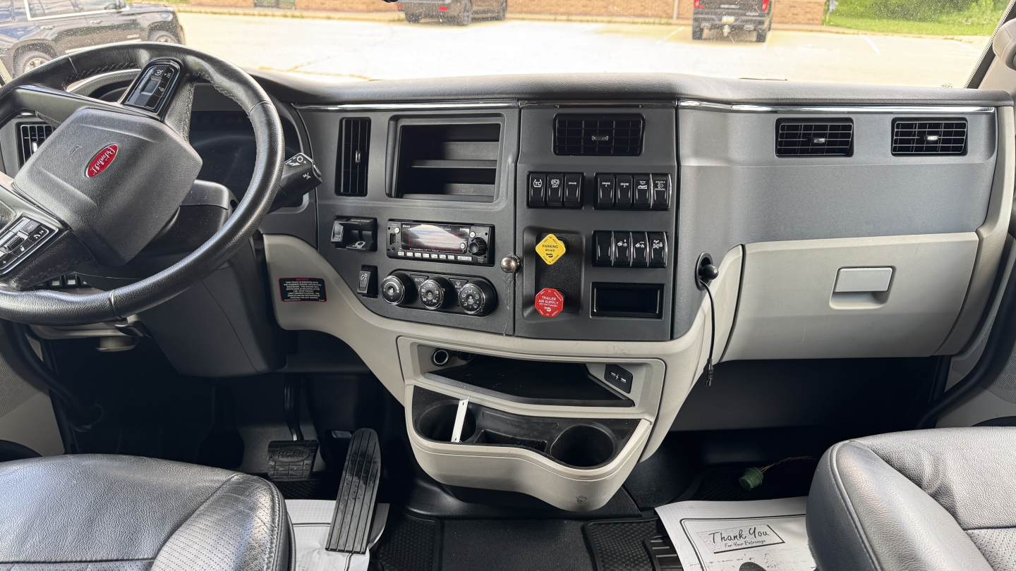 Peterbilt 579 cab interior dashboard view with steering wheel, center console, and instrument cluster; visible controls for climate and media, USB, and storage pockets.