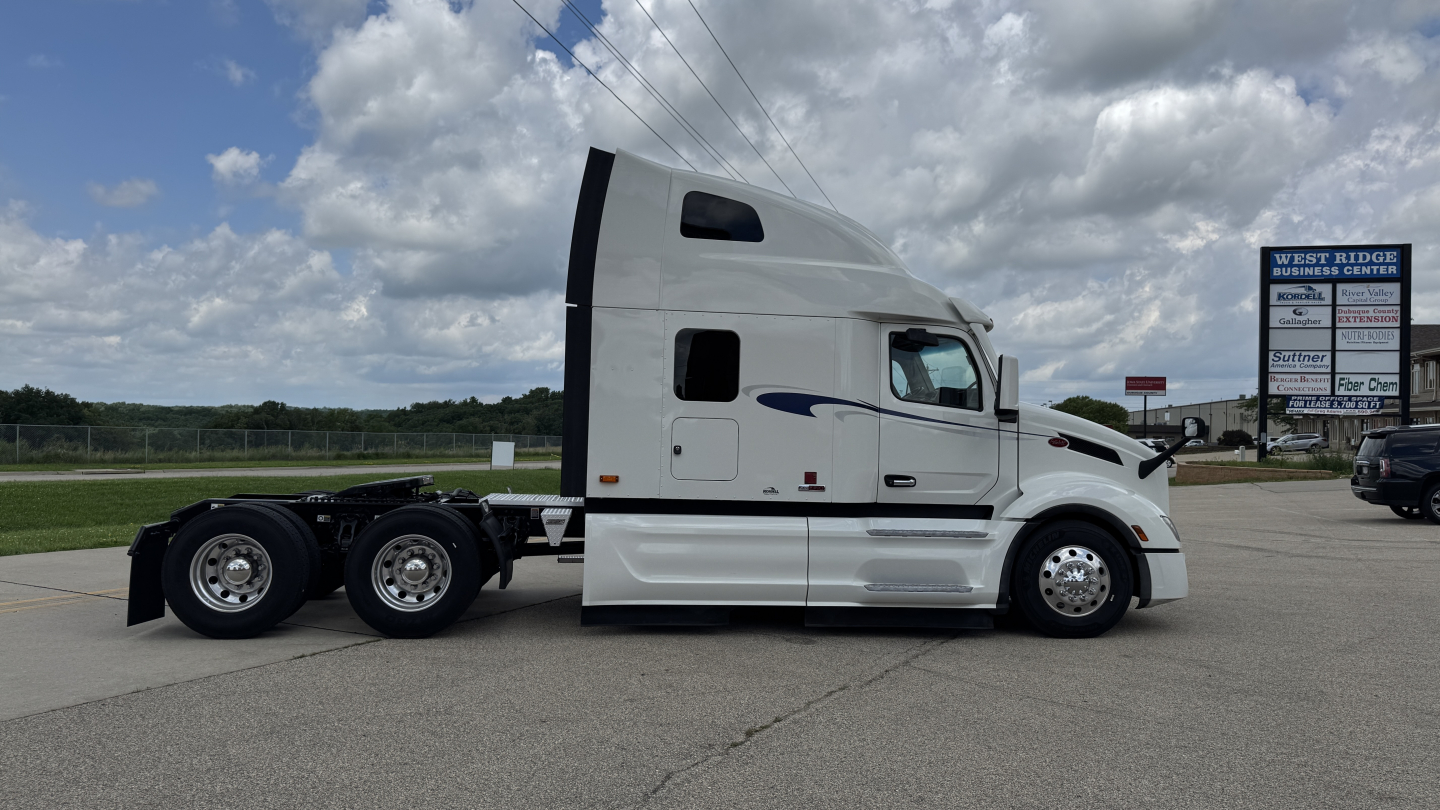 Peterbilt 579 conventional sleeper truck side profile showing white cab and dual rear axles with chrome wheels