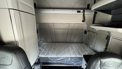 Peterbilt 579 sleeper cab interior showing bed area with quilted mattress pad and storage compartments.