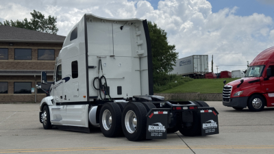 Peterbilt 579 tractor cab rear view showing fifth wheel and dual rear axles, white paint, chrome fuel tanks, and dual mud flaps.