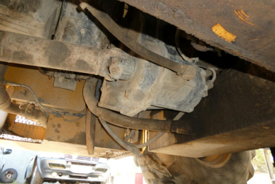 Industrial truck lift undercarriage showing hydraulic hose, metal linkages, and a worn drivetrain component with wiring tape visible.