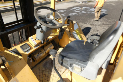 Operator seat and steering wheel of a yellow forklift/truck lift showing control panel and lever with worn floor mat.