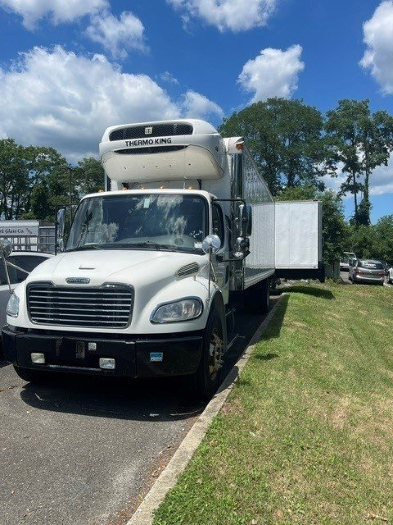 Freightliner M2 106 refrigerated truck with Thermo King unit on cab roof, white cab, side cooling box, parked on grassy lot.
