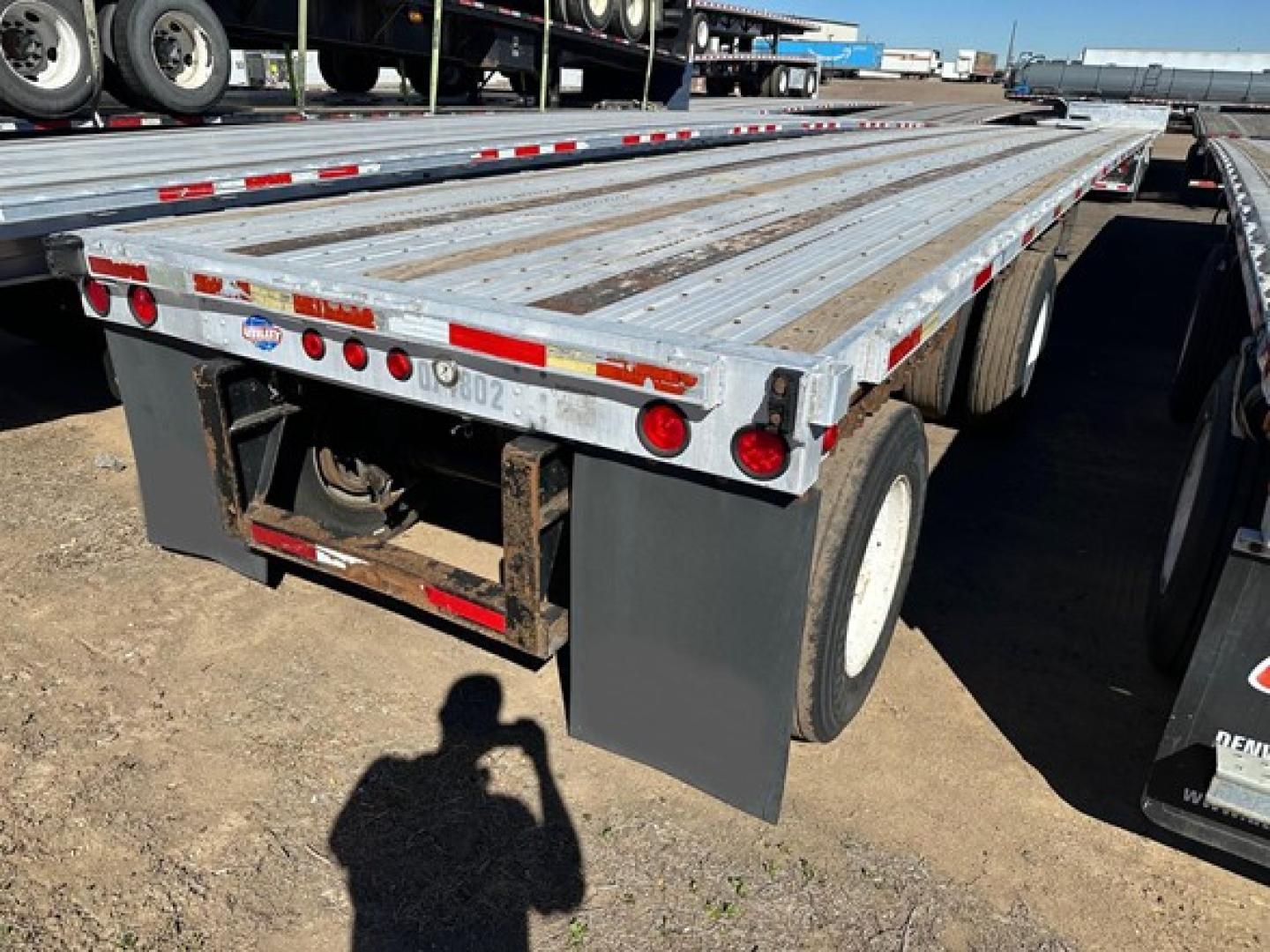 Flatbed trailer with aluminum deck showing rear view and tandem axles, utility logo and taillights visible.