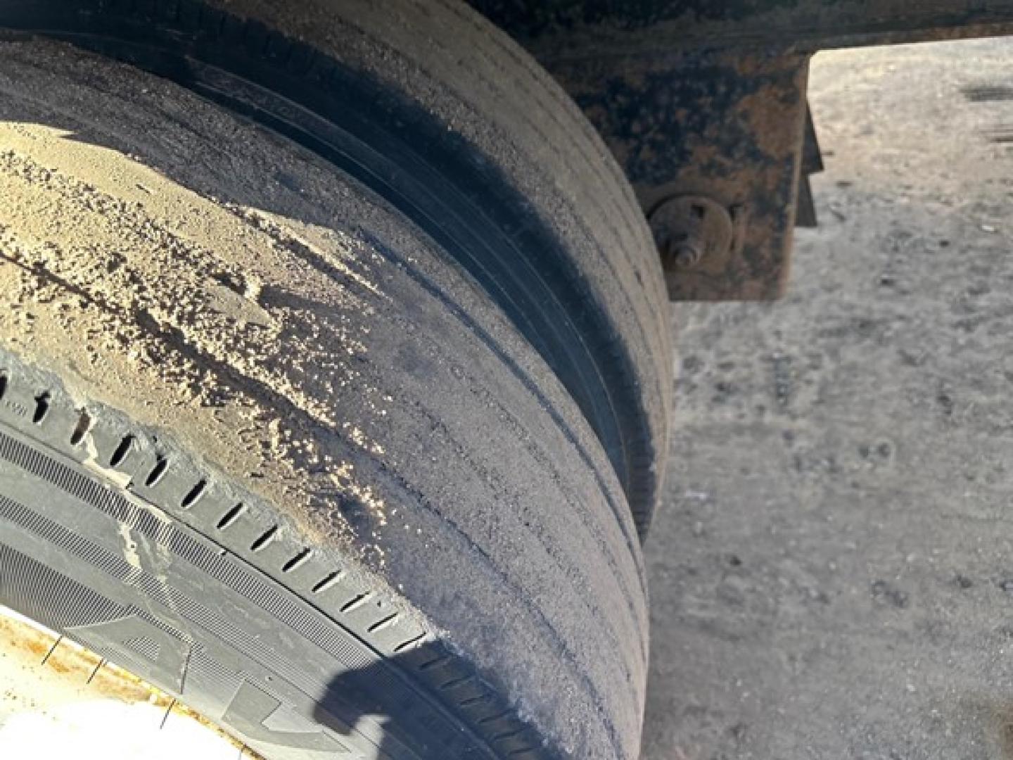 Flatbed trailer wheel and mud-covered tire view showing dual wheel assembly and part of frame.