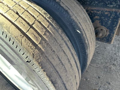 Tire sidewall and wheel area of a utility trailer showing dirt and tread marks; portion of chassis visible in background.
