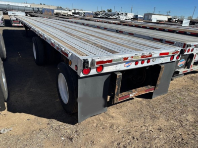 Flatbed trailer platform with dual rear axles and mud flaps, aluminum decking, reflective tape, and stake pockets.