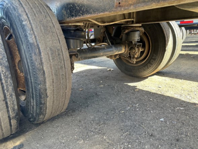 Trailer undercarriage showing dual rear axles and tires; metal suspension components and leaf springs visible.