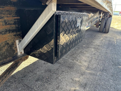 Underbody view of a utility spread air combo flatbed trailer showing a diamond plate toolbox under the deck and support framing.